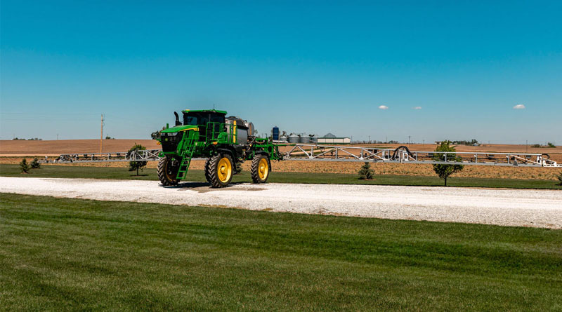 A self-propelled sprayer with an extended boom beside farmland.